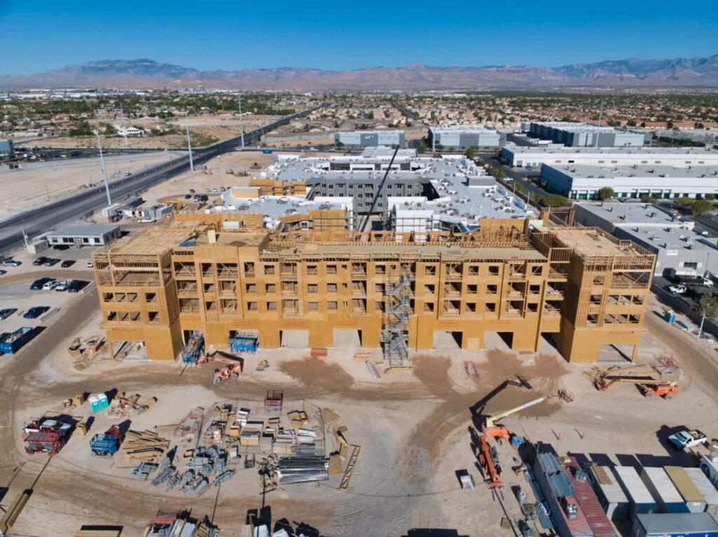 Aerial view of a large multi-story building under construction in Las Vegas—a city that's not just about bright lights and casinos, but also a hotspot for drone photography—surrounded by construction materials, vehicles, roads, and mountains in the background.