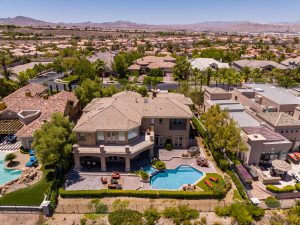 Aerial view of a large, modern house with a backyard pool, patio seating, and lush landscaping—showcasing how mastering aerial photography for real estate success captures stunning surroundings and mountain views in the distance.