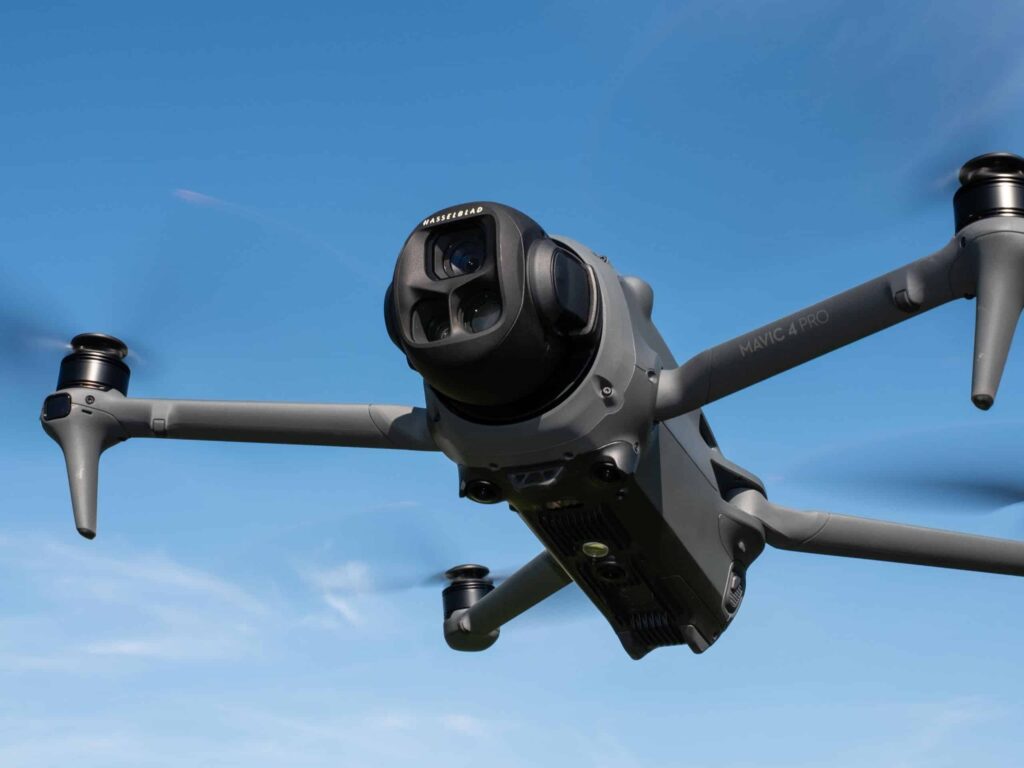 A close-up view of a DJI Mavic 4 Pro drone with four propellers flying against a clear blue sky, highlighting its camera and front sensors—perfect for capturing stunning drone photography.
