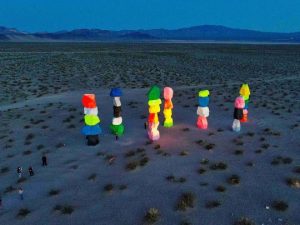 Brightly colored stacked boulders form tall sculptures in a desert landscape at dusk, surrounded by mountains and sparse vegetation, with a few people nearby—an iconic scene for any Las Vegas photo gallery.