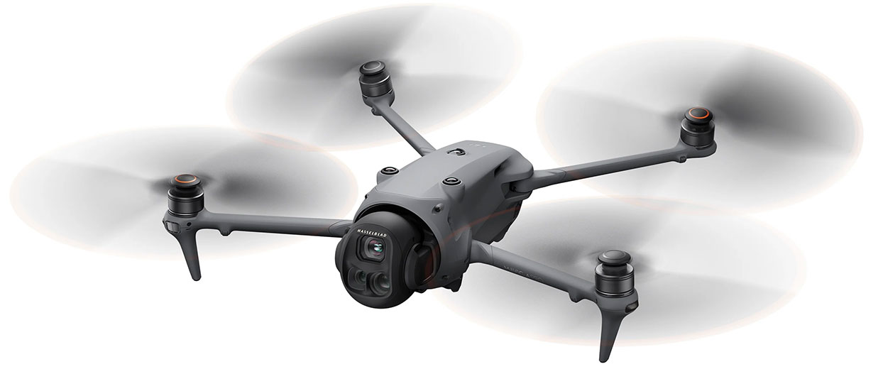 A sleek gray quadcopter drone with four spinning propellers and a camera mounted on the front, shown mid-flight against a white background.