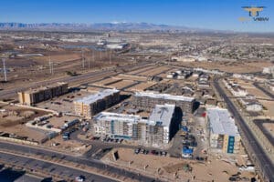 Aerial view of a residential construction site in a desert city, featuring sky-high-precision-revolutionizing-construction-projects-with-drone-imaging; apartment buildings, roads, sparse vegetation, and distant mountains under a clear blue sky.